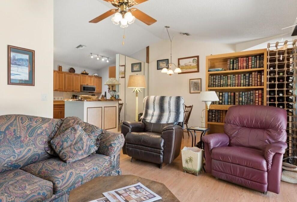 A living room features a paisley sofa, two armchairs, a wooden bookshelf, and an open kitchen — 6287 N Mirror Lake Drive, Sebastian FL 32958, SEBASTIAN, FL