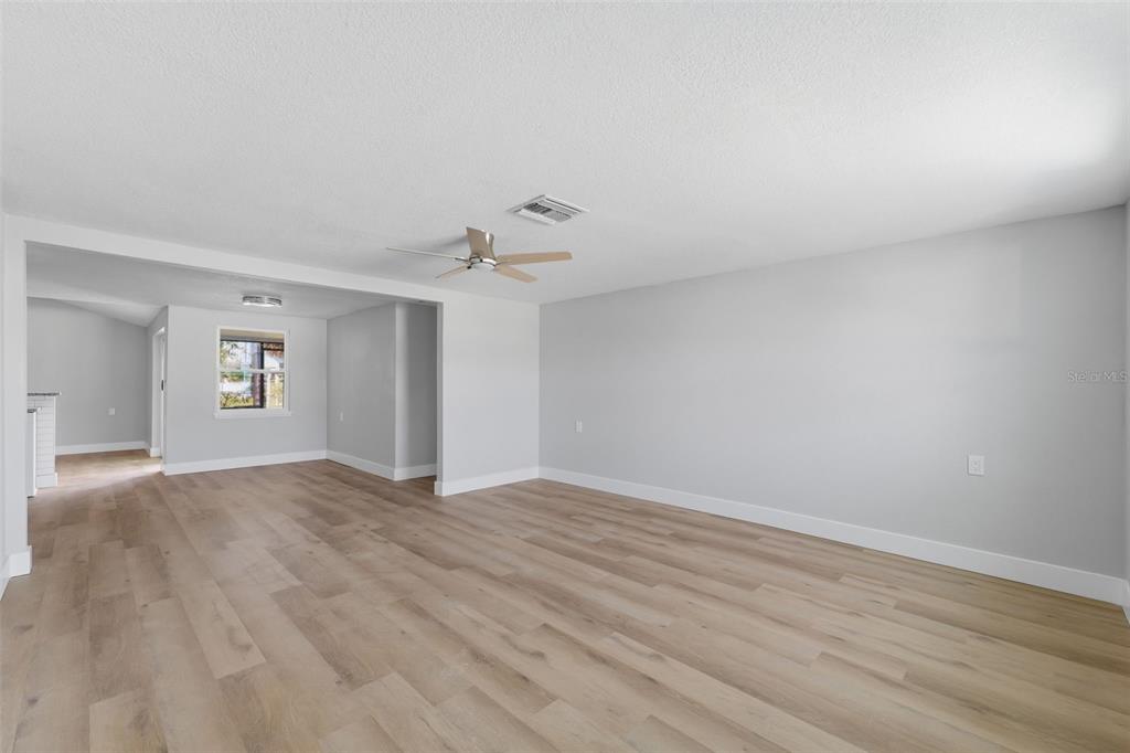 A spacious, light-filled living area features light wood-look flooring, gray walls, and a ceiling fan — 7608 YACHTSMAN DRIVE, HUDSON, FL