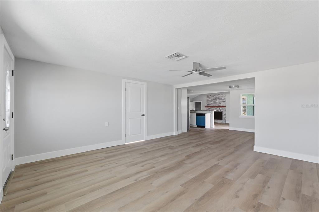 A bright, open-concept living area features light wood-look flooring, white walls, and a ceiling fan — 7608 YACHTSMAN DRIVE, HUDSON, FL