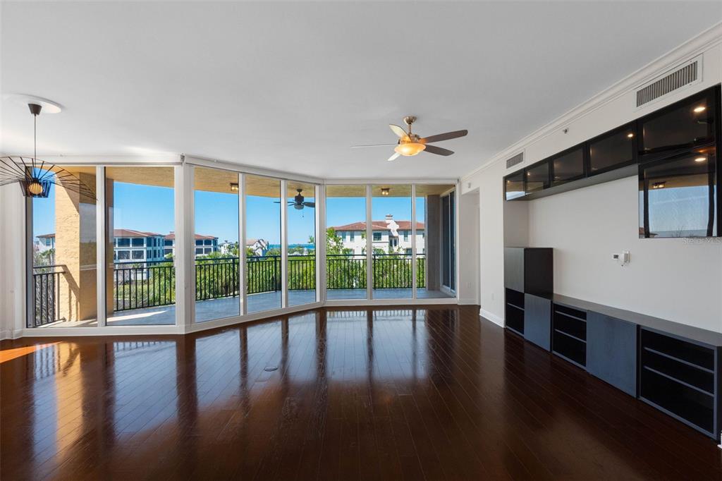 A living room with dark hardwood floors, a ceiling fan, and floor-to-ceiling windows overlooking balconies — 5823 BOWEN DANIEL DRIVE UNIT 401, TAMPA, FL
