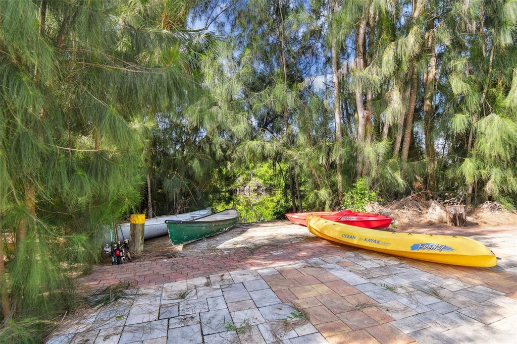 A paved patio area features several kayaks and a canoe near a wooded waterfront — 5909 MOHR ROAD, TAMPA, FL