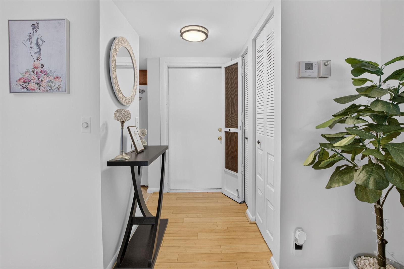 A bright entryway features light wood flooring, a console table, a mirror, and a door — 11 Willowbrook Lane # 204, Delray Beach FL 33446, DELRAY BEACH, FL