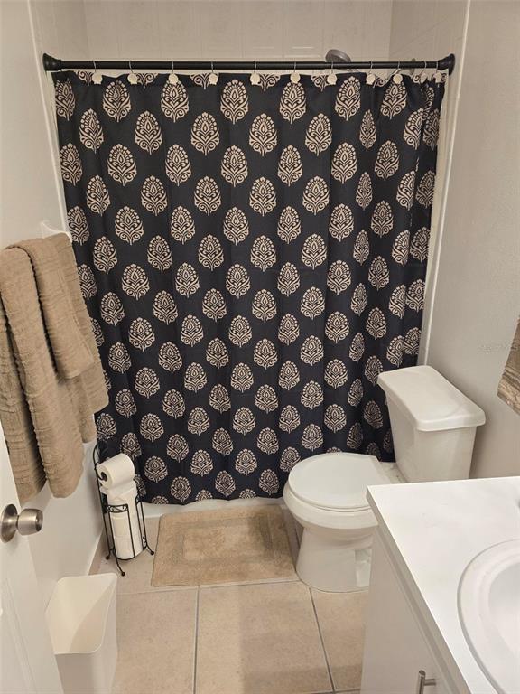 A bathroom features a patterned shower curtain, a white toilet, and a vanity with tile flooring — 136 KNOTTS LANE, KISSIMMEE, FL