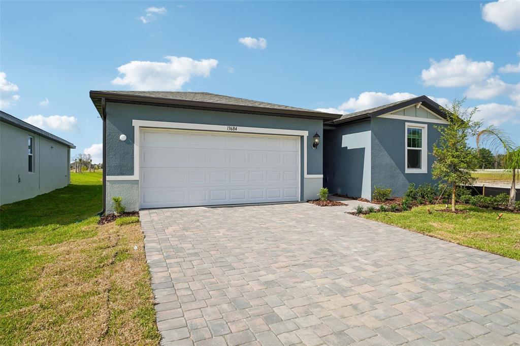 A single-story house with a blue stucco exterior, a two-car garage, and a paver driveway — 13684 UMBER FOREST STREET, HUDSON, FL