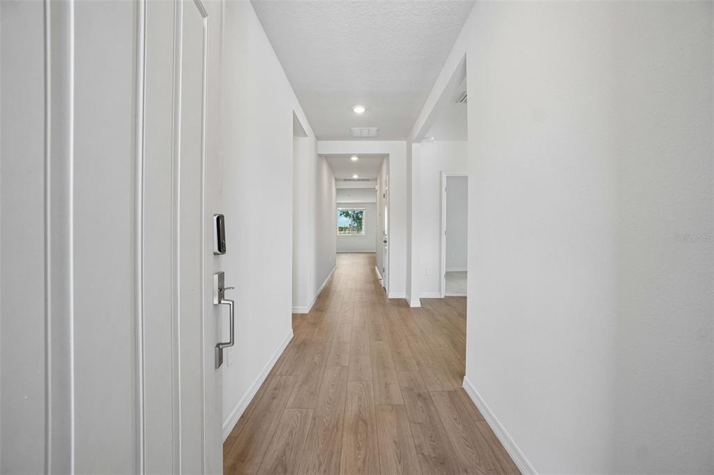 A long hallway with light wood-look flooring leads to a window at the far end — 13684 UMBER FOREST STREET, HUDSON, FL