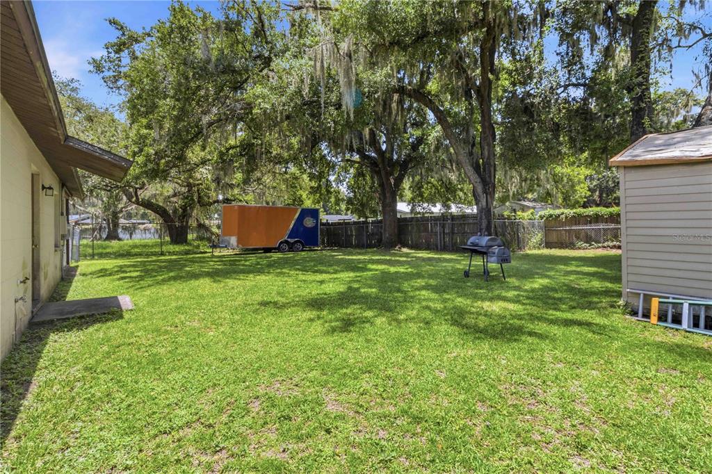 A grassy backyard features a storage shed, a charcoal grill, and a parked utility trailer — 2113 OAKVIEW LANE, PLANT CITY, FL