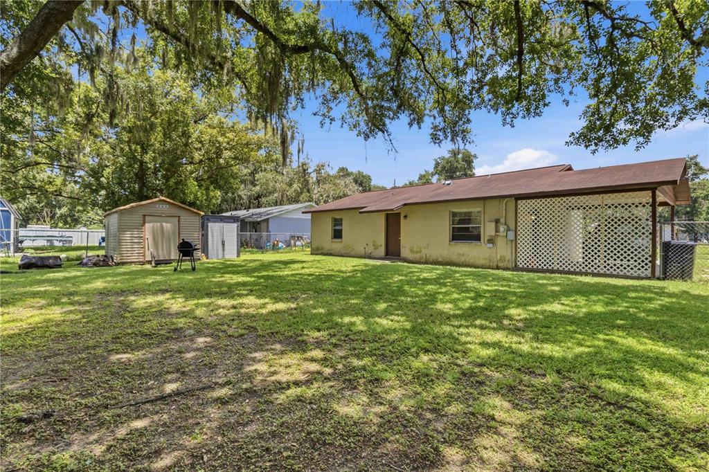 The backyard of a single-story house features a lawn, two storage sheds, and a patio — 2113 OAKVIEW LANE, PLANT CITY, FL