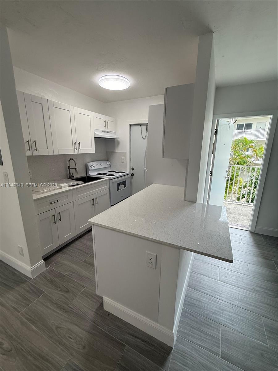 A kitchen features white cabinets, quartz countertops, a breakfast bar, and gray wood-look flooring — 1895 Venice Park Dr # B6, Miami FL 33181, MIAMI, FL