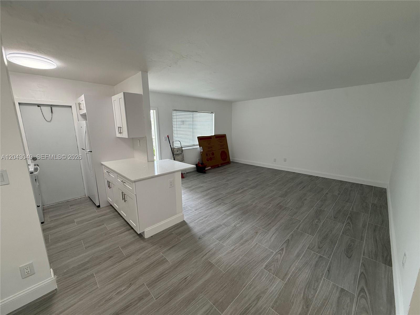 An open-concept room features white cabinetry, a kitchen island, and gray wood-look tile flooring — 1895 Venice Park Dr # B6, Miami FL 33181, MIAMI, FL