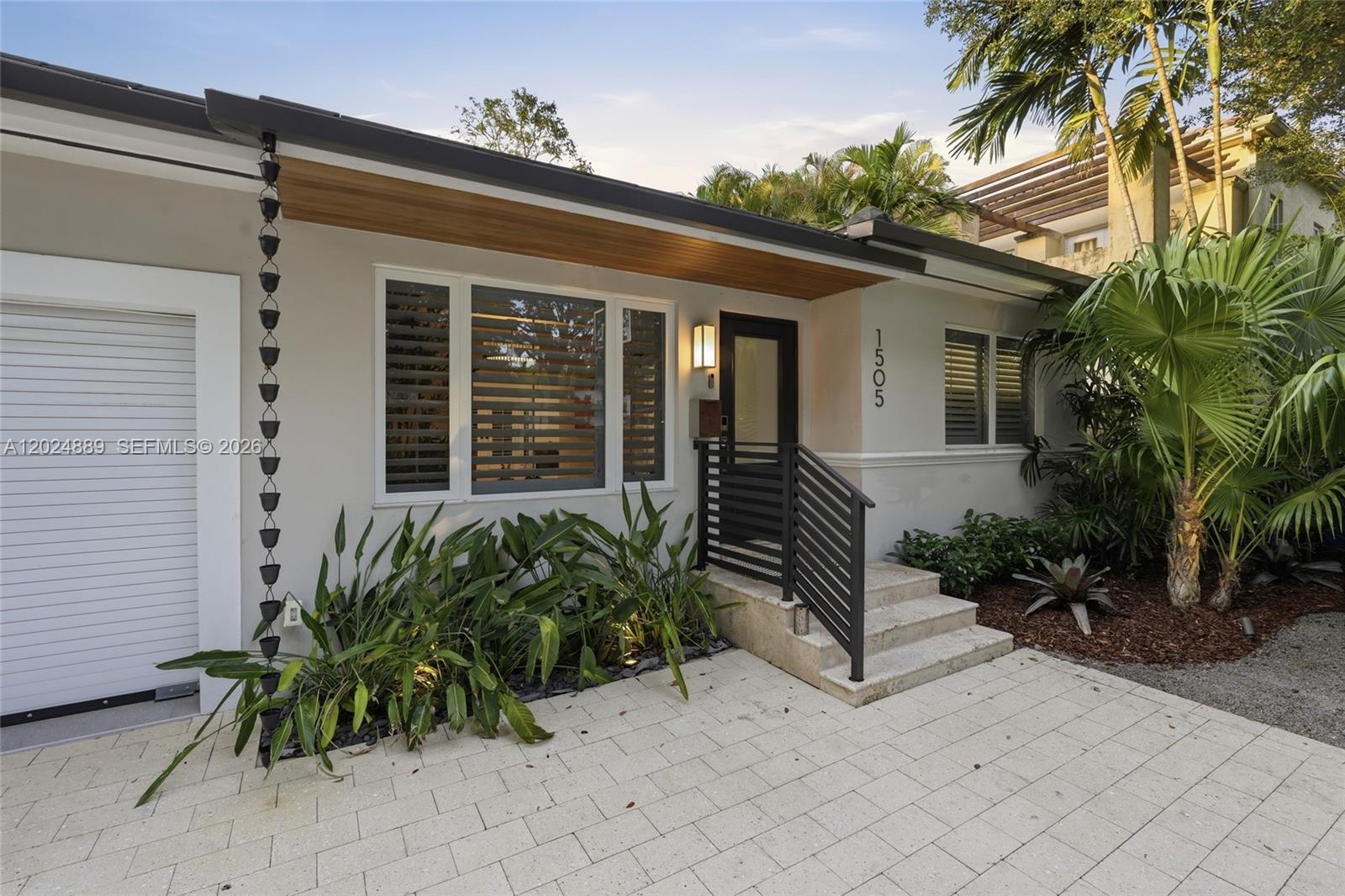 The exterior of a single-story house features a paved driveway, a rain chain, and landscaping — 1505 Robbia Ave, Coral Gables FL 33146, CORAL GABLES, FL
