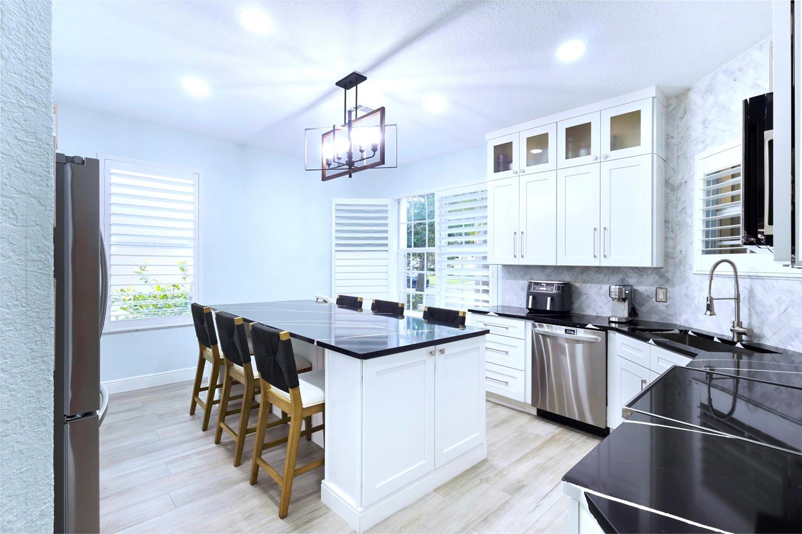 A modern kitchen features white cabinets, black countertops, a large island, and stainless steel appliances — 8070 Murano Circle, Palm Beach Gardens FL 33418, PALM BEACH GARDENS, FL