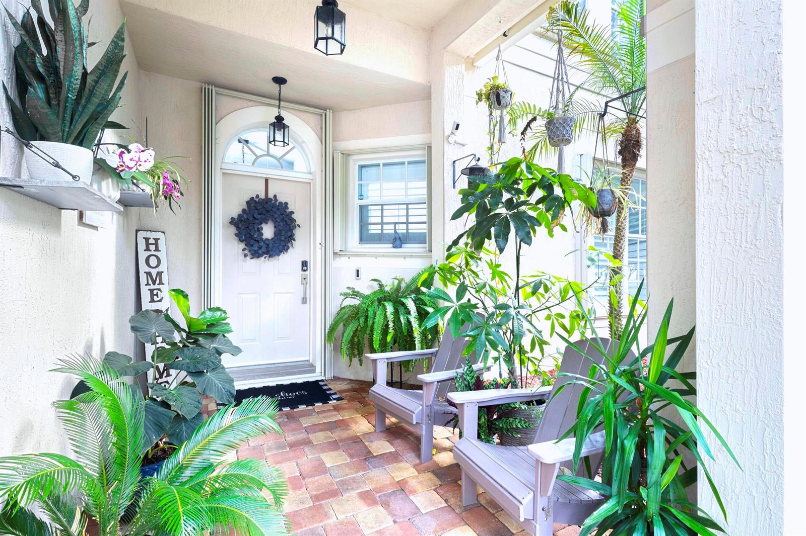A covered front porch features a brick floor, two gray chairs, and numerous potted plants — 8070 Murano Circle, Palm Beach Gardens FL 33418, PALM BEACH GARDENS, FL