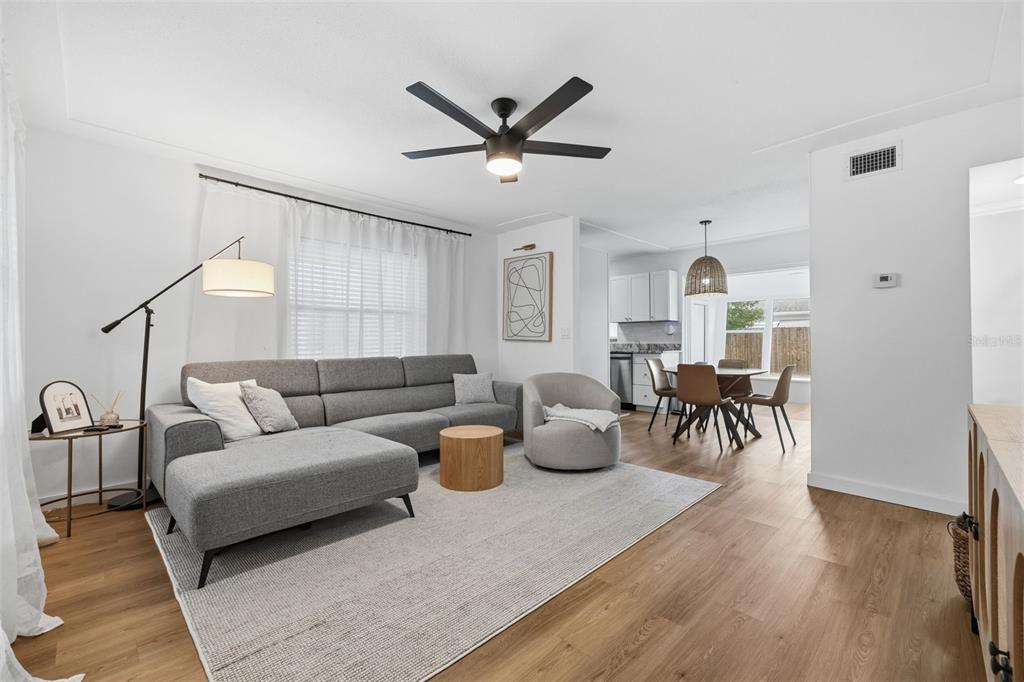 A living room with a gray sectional, round chair, and dining area on wood floors — 9851 52ND STREET N, PINELLAS PARK, FL