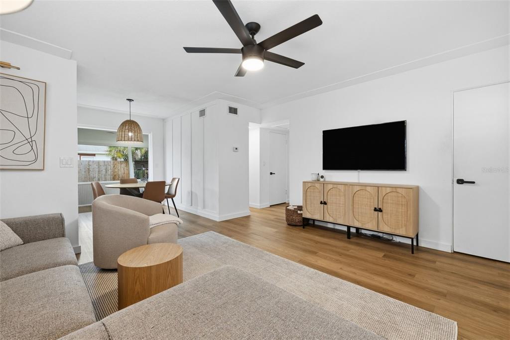 A living room features light wood flooring, a ceiling fan, and a wall-mounted television — 9851 52ND STREET N, PINELLAS PARK, FL