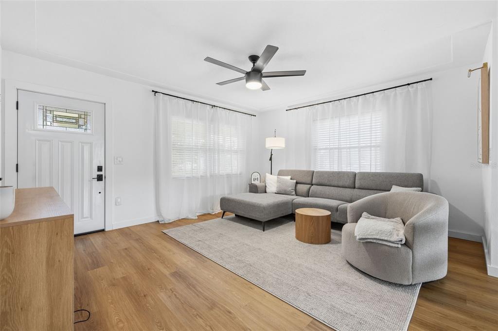 A living room features a gray sectional sofa, a round chair, and wood-look flooring — 9851 52ND STREET N, PINELLAS PARK, FL