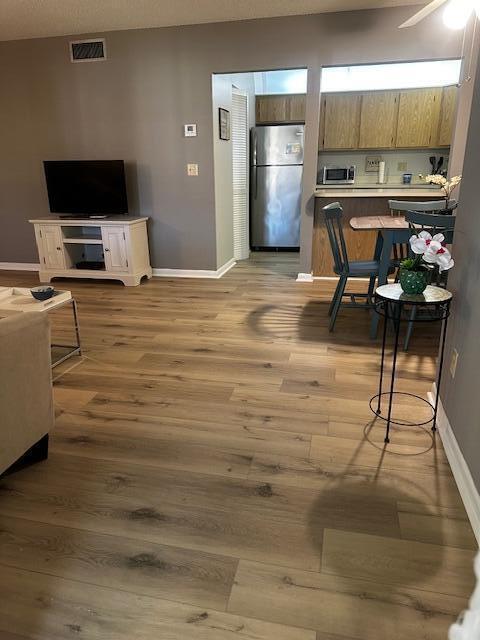 A living room with wood-look flooring leads into a kitchen with stainless steel appliances — 441 Pine Glen Lane # 2, FL 33463, FL