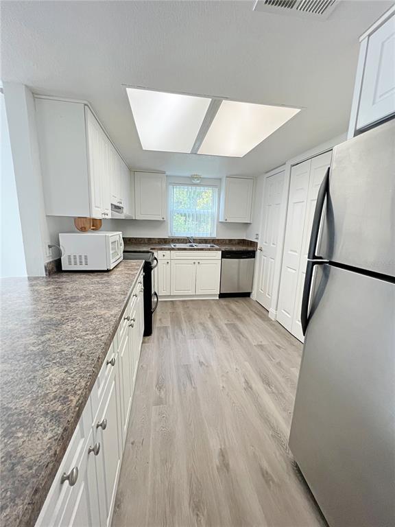 A galley kitchen features white cabinets, dark laminate countertops, stainless steel appliances, and wood-look flooring — 2425 BARLEY CLUB DRIVE UNIT 8, ORLANDO, FL