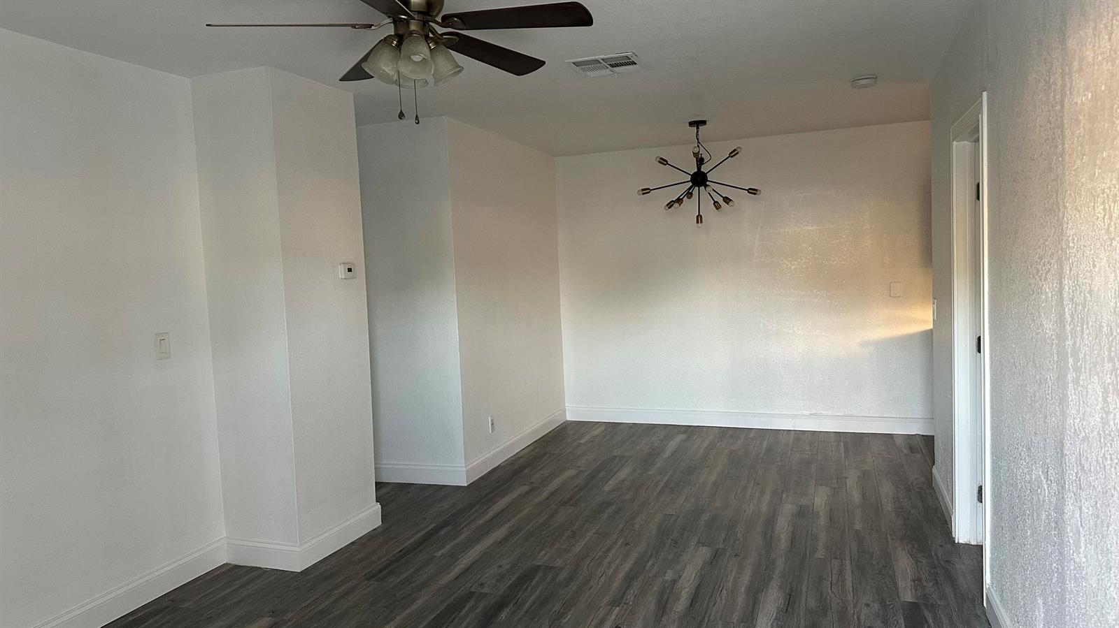An empty room features white walls, gray wood-look flooring, a ceiling fan, and a chandelier — 4628 SW 32nd Drive, West Park FL 33023, WEST PARK, FL