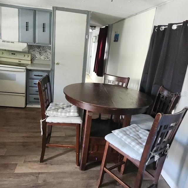 A dining area features a round wooden table, four chairs with cushions, and an adjacent kitchen — 5820 OLIVE DRIVE, NEW PORT RICHEY, FL