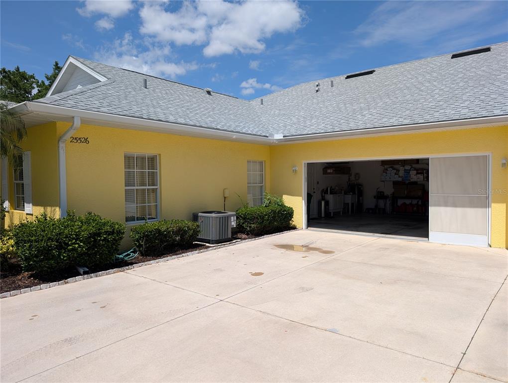 A yellow house exterior features a gray shingled roof, a concrete driveway, and an open garage — 25526 HERITAGE LAKE BOULEVARD, PUNTA GORDA, FL