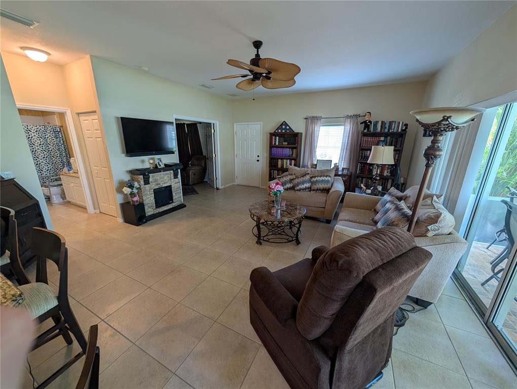 A living room with tile floors, a fireplace, a ceiling fan, and sliding glass doors — 25526 HERITAGE LAKE BOULEVARD, PUNTA GORDA, FL