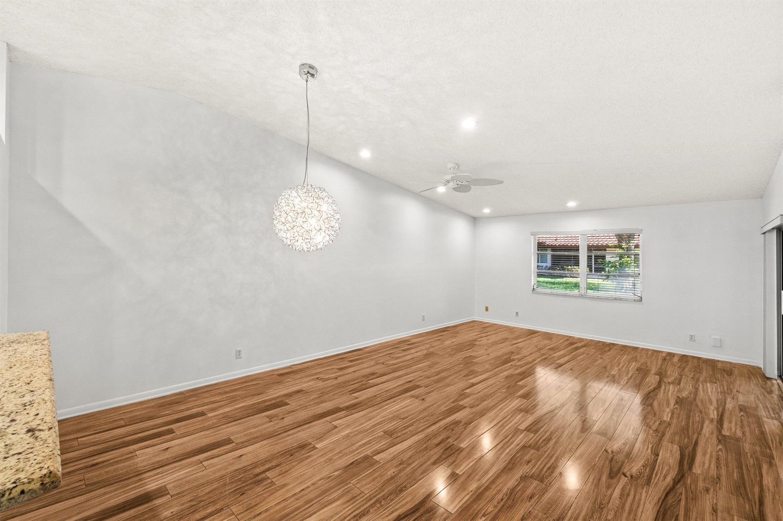 An empty room features wood-look flooring, a modern pendant light, and a ceiling fan — 6079 Millington Way, Delray Beach FL 33484, DELRAY BEACH, FL