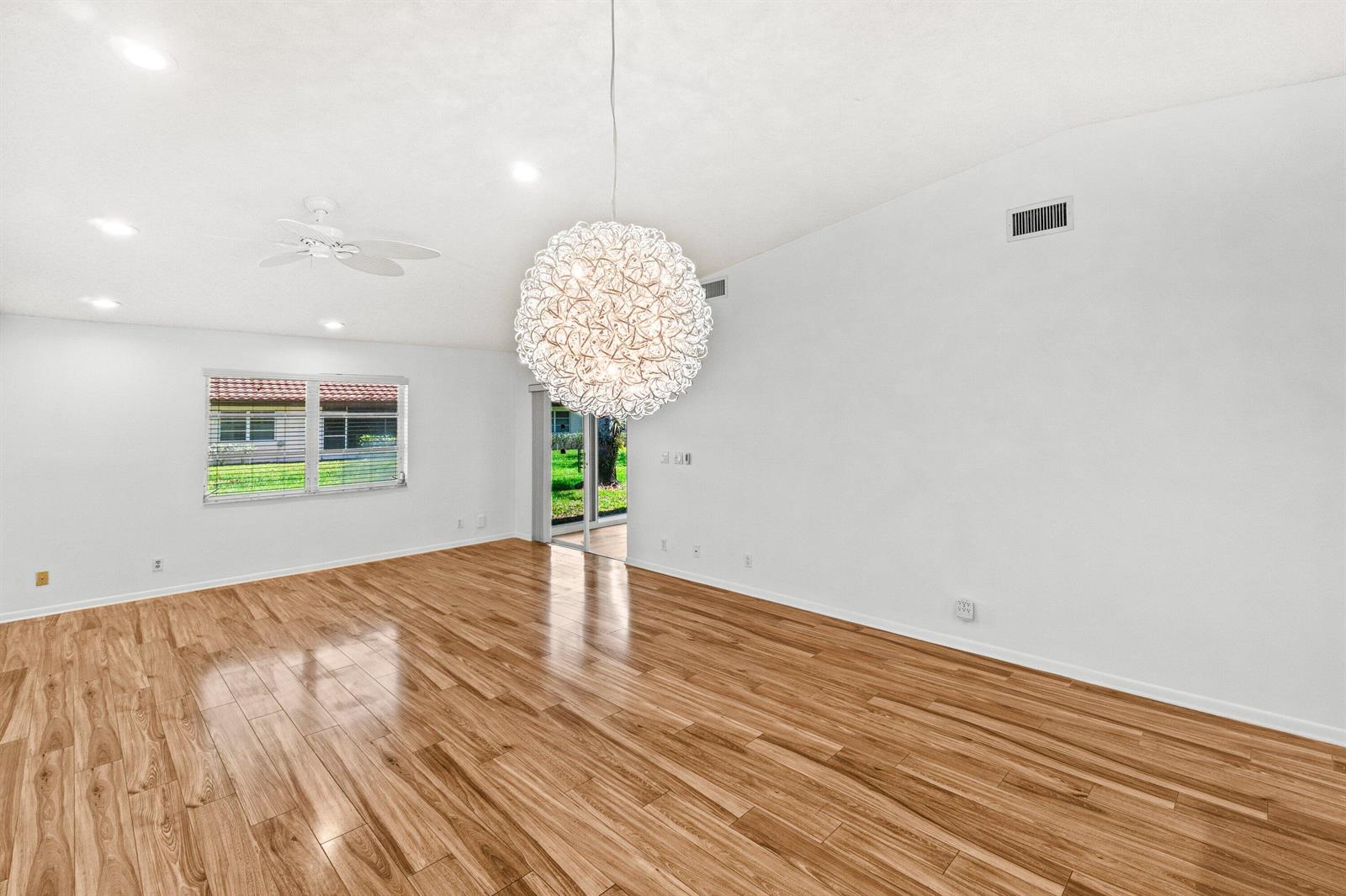 An empty living room features light wood-look flooring, white walls, a ceiling fan, and a chandelier — 6079 Millington Way, Delray Beach FL 33484, DELRAY BEACH, FL