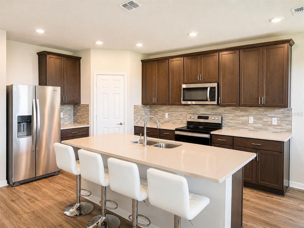 A kitchen features dark wood cabinets, stainless steel appliances, a quartz island, and white stools — 196 TOWNS CIRCLE, HAINES CITY, FL