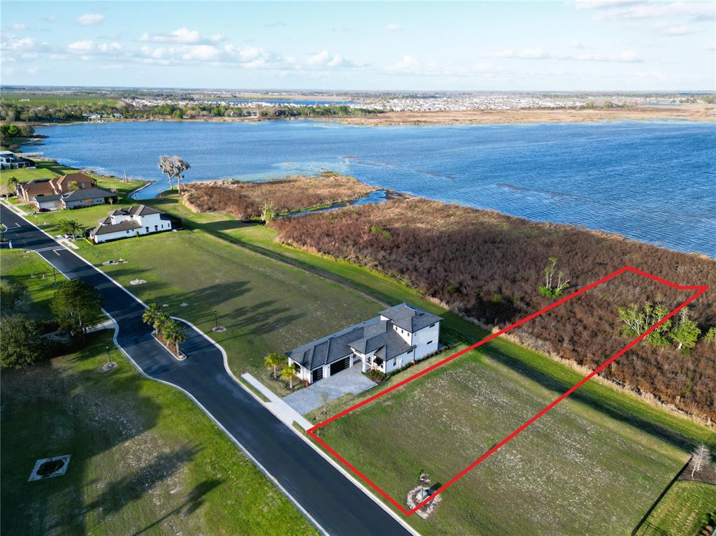 An aerial view shows a vacant rectangular lot outlined in red next to a modern house — 332 CALADIUM AVENUE, LAKE ALFRED, FL