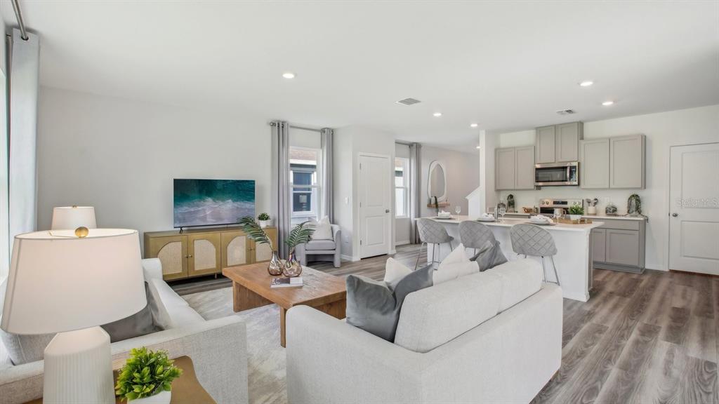 An open-concept living room and kitchen featuring light gray cabinetry and wood-look flooring — 13277 TABLE ROCK LANE, DADE CITY, FL