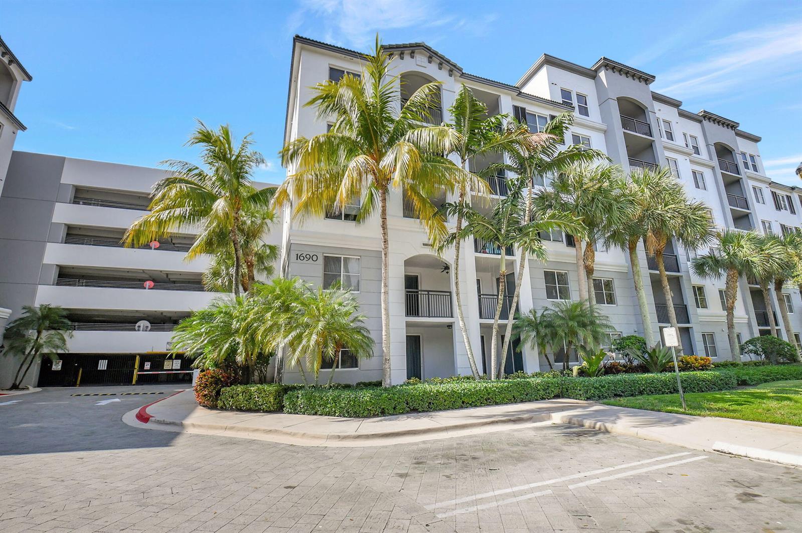 A multi-story apartment building with a parking garage and palm trees in the foreground — 1660 Renaissance Commons Boulevard # 2424, Boynton Beach FL 33426, BOYNTON BEACH, FL