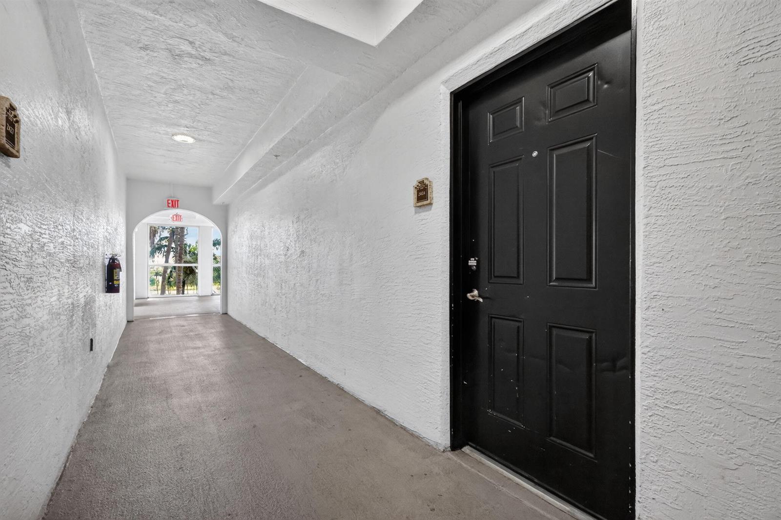 A black door stands at the end of a white hallway leading to an exit — 1660 Renaissance Commons Boulevard # 2424, Boynton Beach FL 33426, BOYNTON BEACH, FL