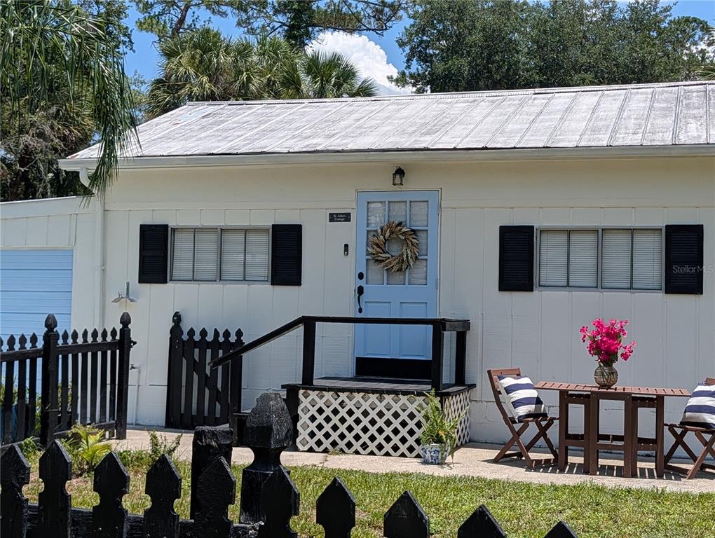 A white cottage with a light blue door, black shutters, and a small wooden porch — 55914 BAY ROAD, ASTOR, FL