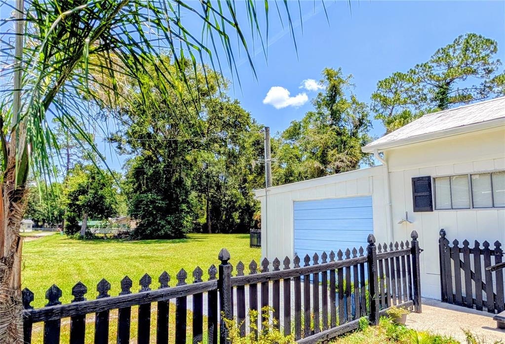 A black picket fence borders a grassy yard next to a house with a garage — 55914 BAY ROAD, ASTOR, FL