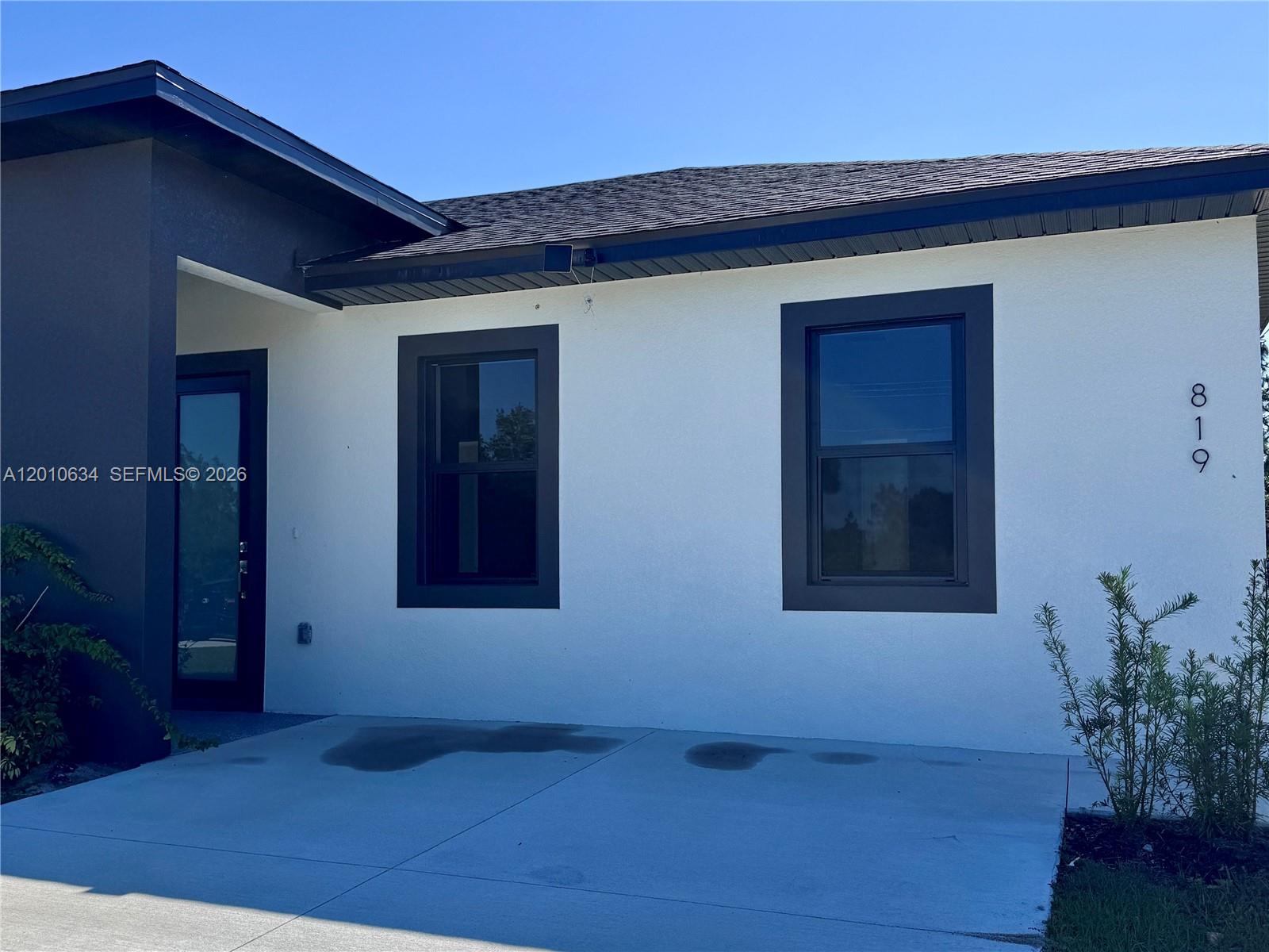 The exterior of a white house features dark trim, two windows, and a front entrance — 819 Eisenhower Blvd # 819, Lehigh Acres FL 33974, LEHIGH ACRES, FL