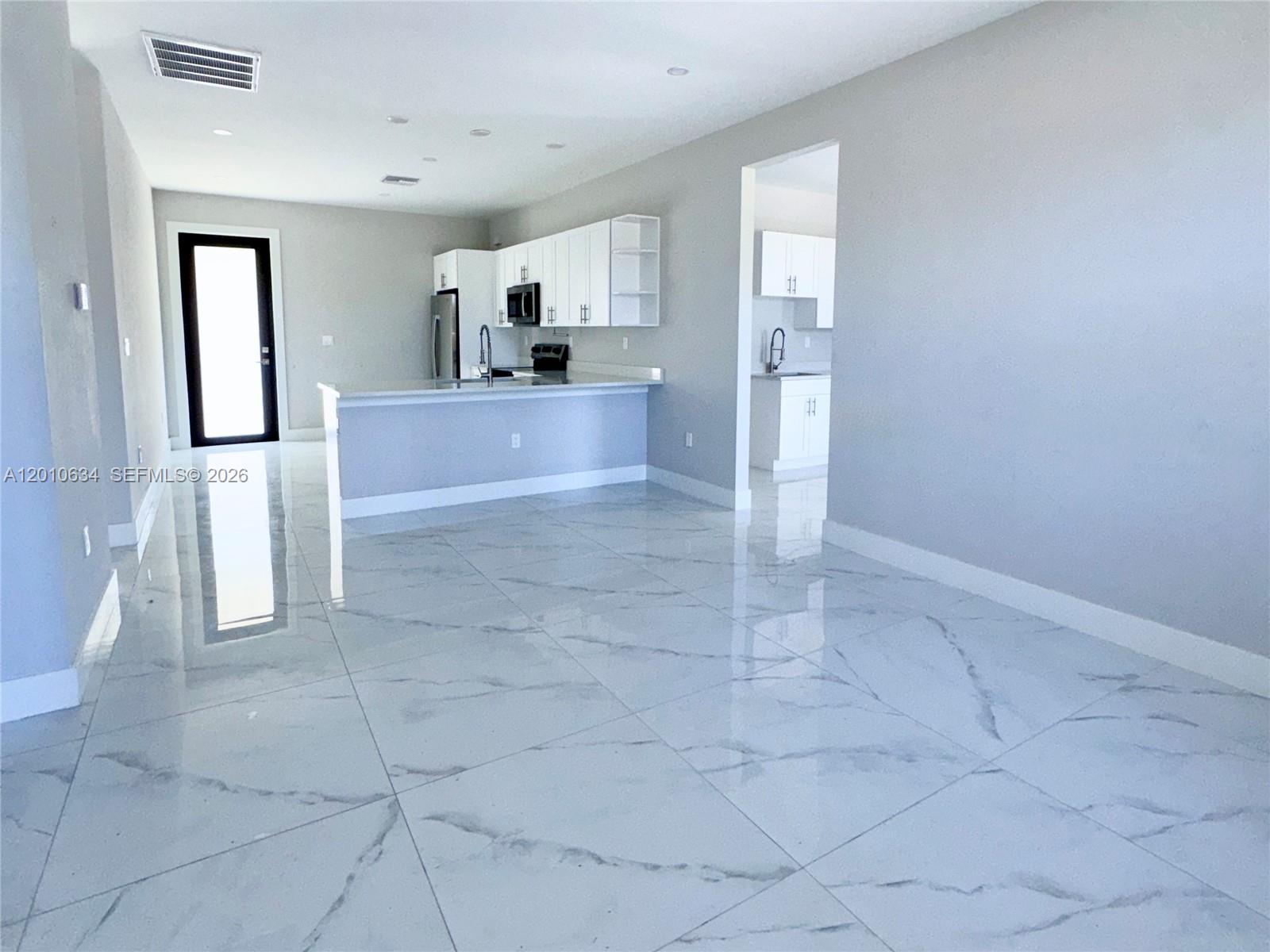 A modern kitchen features white cabinets, a breakfast bar, and glossy marble-patterned tile floors — 819 Eisenhower Blvd # 819, Lehigh Acres FL 33974, LEHIGH ACRES, FL