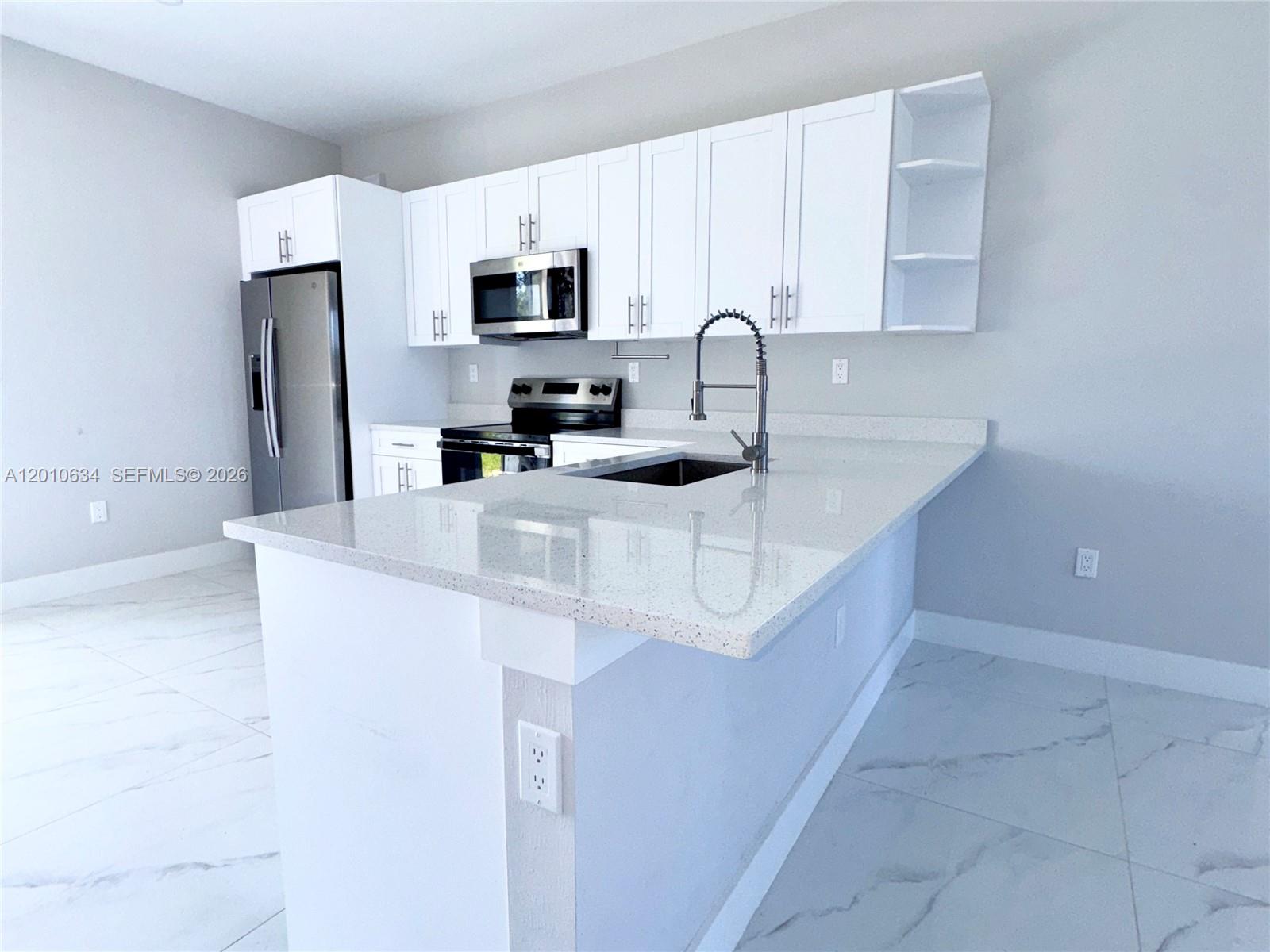 A modern kitchen features white cabinets, stainless steel appliances, and a white quartz countertop island — 819 Eisenhower Blvd # 819, Lehigh Acres FL 33974, LEHIGH ACRES, FL