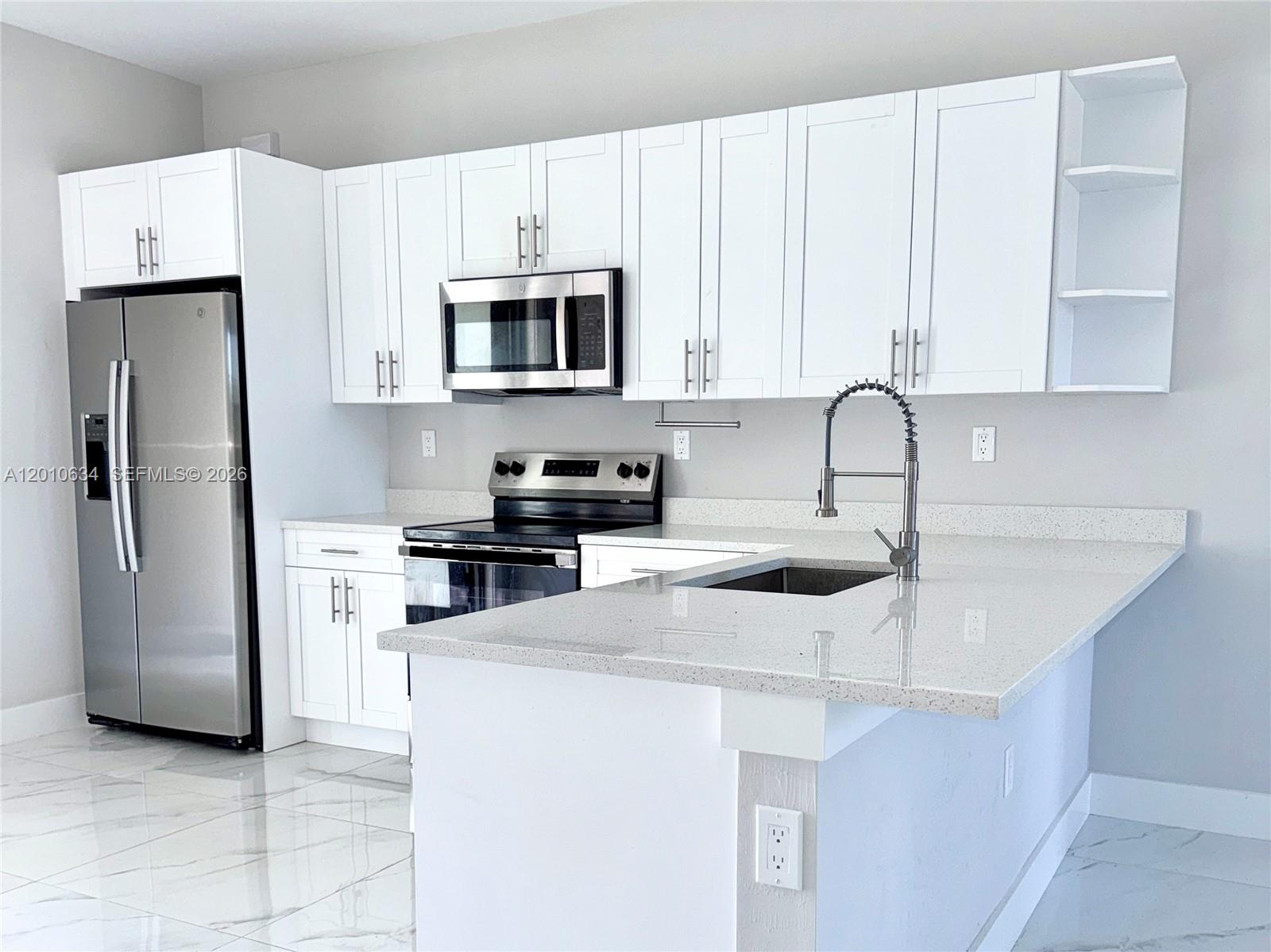 A kitchen features white cabinets, stainless steel appliances, quartz countertops, and light tile flooring — 819 Eisenhower Blvd # 819, Lehigh Acres FL 33974, LEHIGH ACRES, FL
