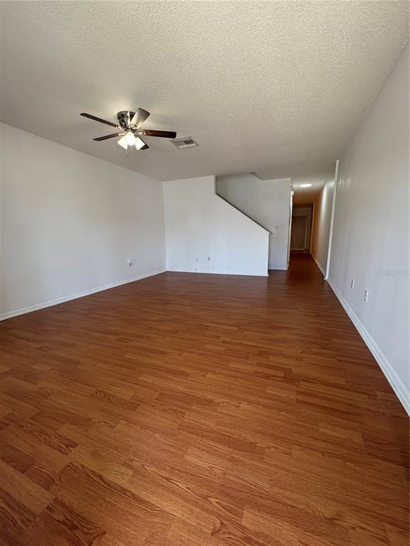 An empty living room features wood-look flooring, a ceiling fan, and a staircase — 1324 KELRIDGE PLACE, BRANDON, FL