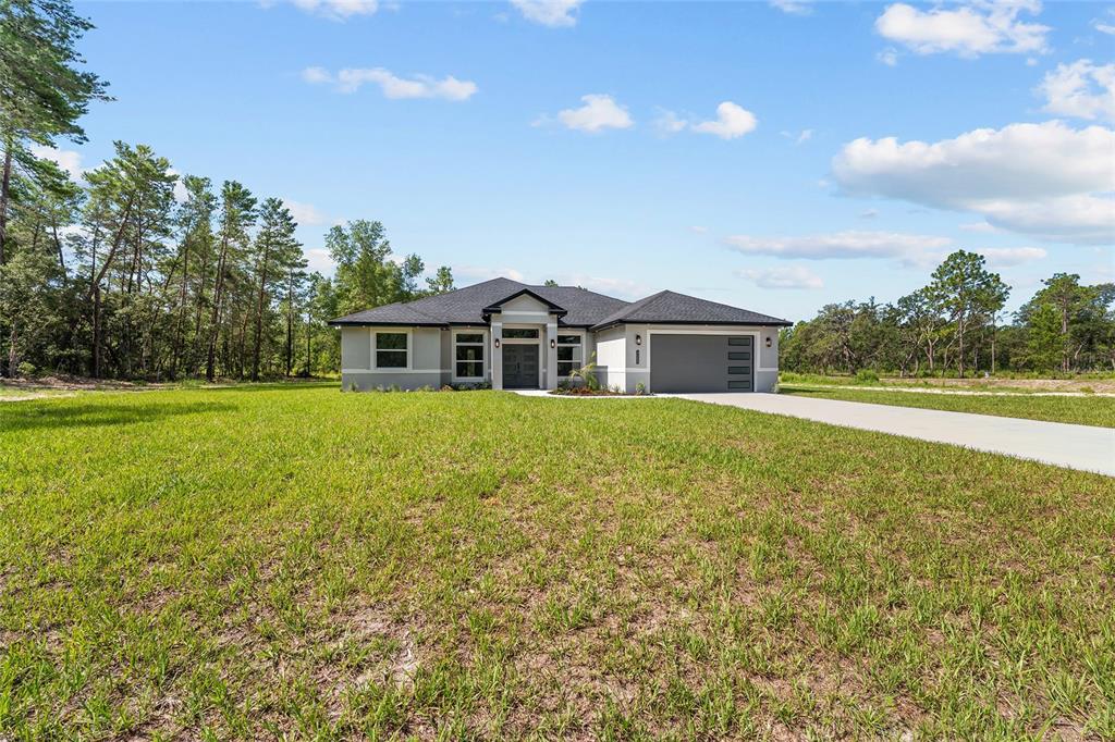 A single-story house sits on a large, sandy lot surrounded by trees under a blue sky — 4660 SW 179TH PLACE, OCALA, FL