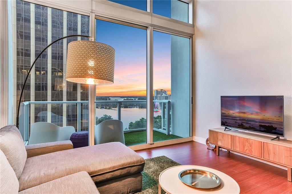 A living room with a sectional sofa, television, and floor-to-ceiling windows overlooking a lake — 150 E ROBINSON STREET UNIT 817, ORLANDO, FL
