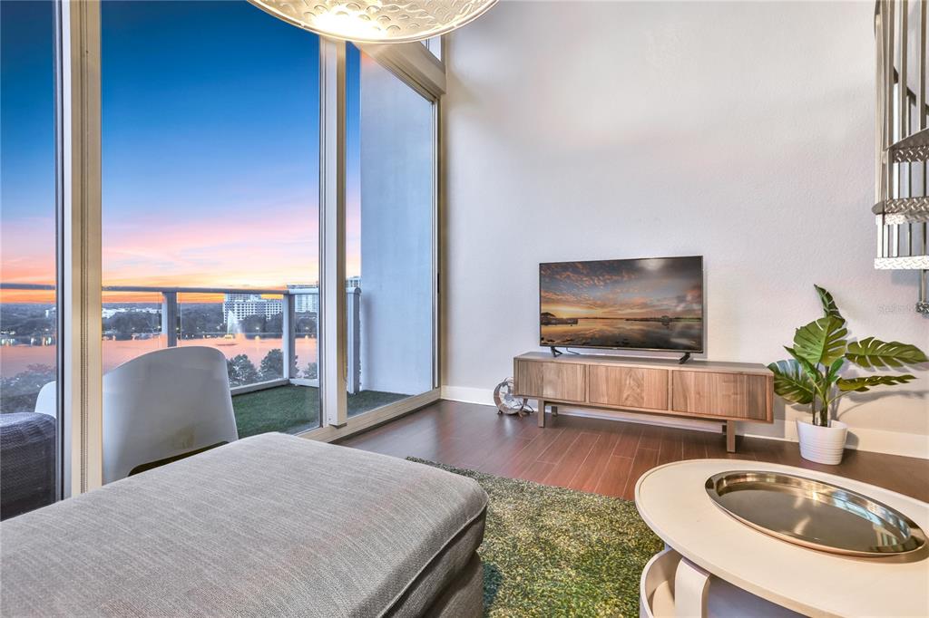A living room features a television on a wooden console, a balcony, and lake views — 150 E ROBINSON STREET UNIT 817, ORLANDO, FL