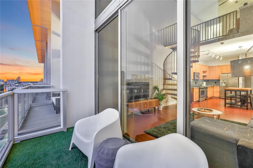 A balcony with artificial turf overlooks a sunset view next to a modern apartment interior — 150 E ROBINSON STREET UNIT 817, ORLANDO, FL