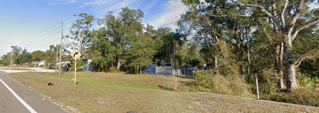 A grassy, tree-lined vacant lot sits next to a road with a curve warning sign — 13818 & 13836 US HIGHWAY 41, SPRING HILL, FL