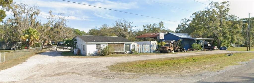 A white building and a blue workshop sit on a gravel lot with trees nearby — 13818 & 13836 US HIGHWAY 41, SPRING HILL, FL