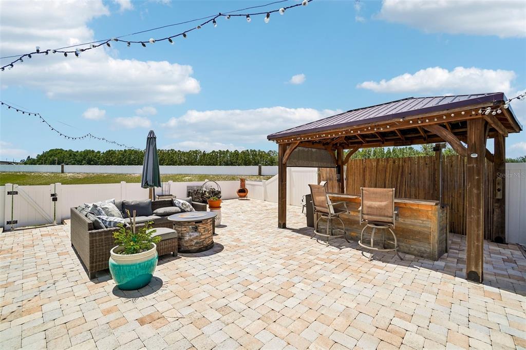 A paved patio features a wooden gazebo bar, outdoor seating, and string lights under a sky — 15792 DURANGO CIRCLE, BROOKSVILLE, FL