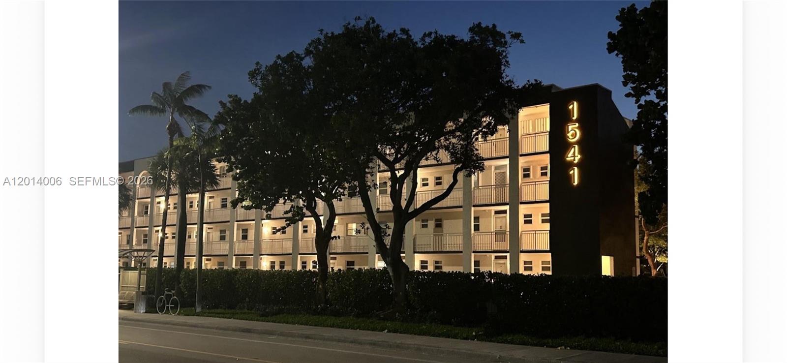 A multi-story apartment building exterior is illuminated at night with a large address number displayed — LAUDERDALE BY THE SEA, FL