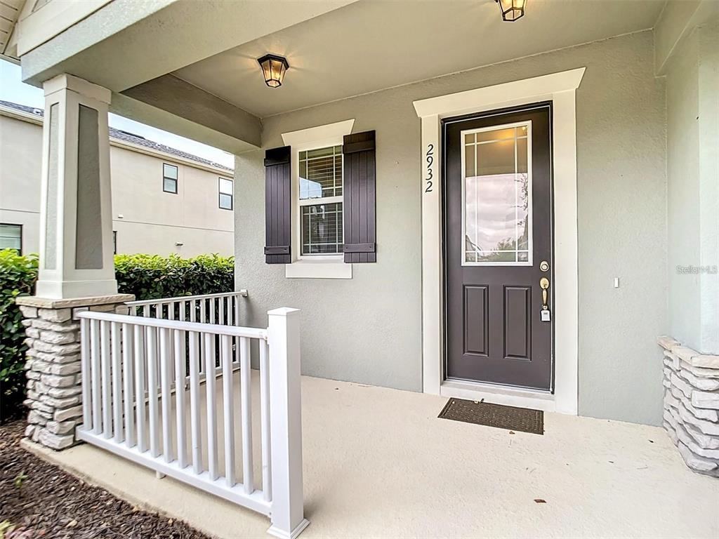 A covered front porch features a dark gray door, white railings, and stone pillar accents — 2932 CELLO LANE, KISSIMMEE, FL