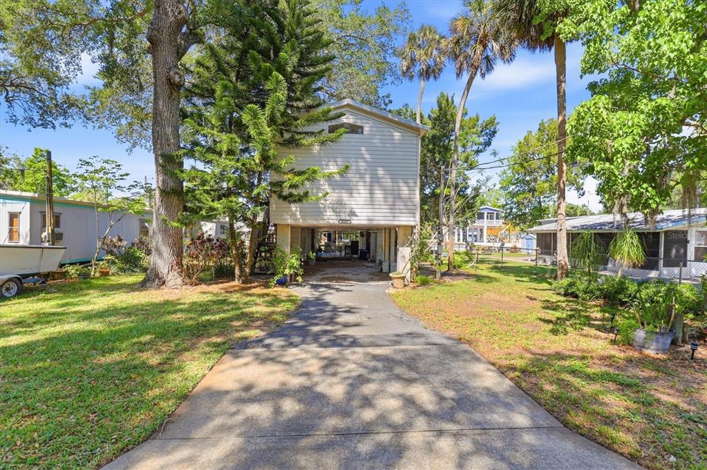 A stilt-raised house with light siding stands at the end of a concrete driveway — 6169 WAVERLY ROAD, WEEKI WACHEE, FL