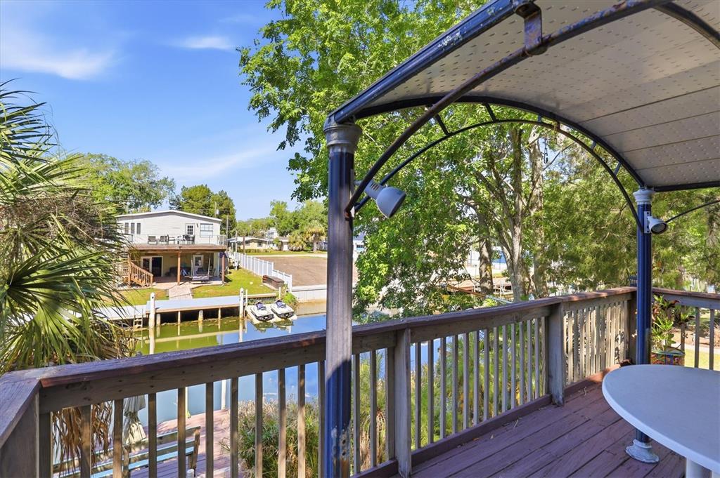 A wooden deck with a metal-framed canopy overlooks a canal and a neighboring house — 6169 WAVERLY ROAD, WEEKI WACHEE, FL